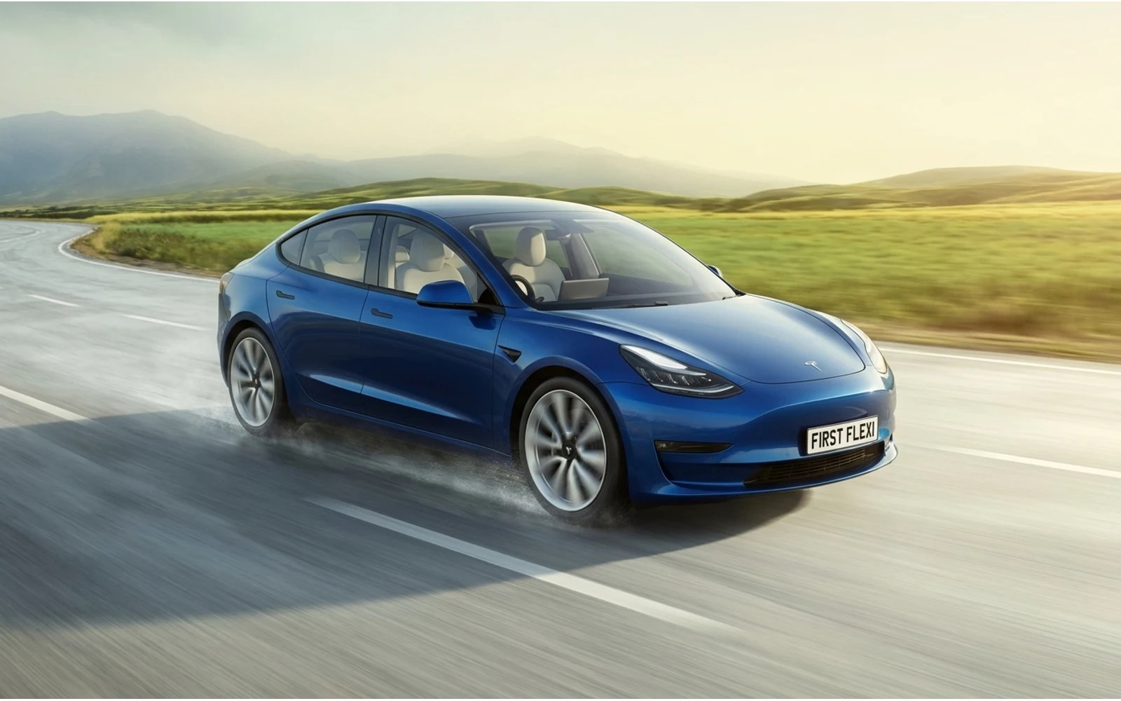 Blue Tesla drives on a wet road past grassy fields and hills.