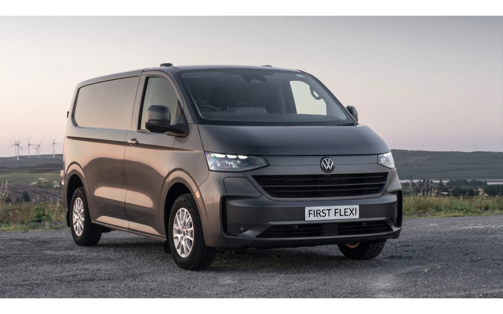 A dark grey Volkswagen Transporter Transporter parked on a gravel surface with windmills in the background.
